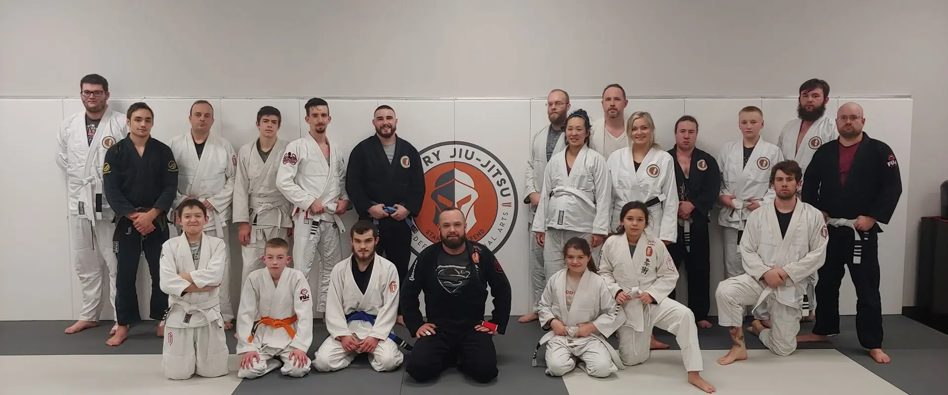 The Sentry Jiu-Jitsu team gathered on the mats in front of the academy logo